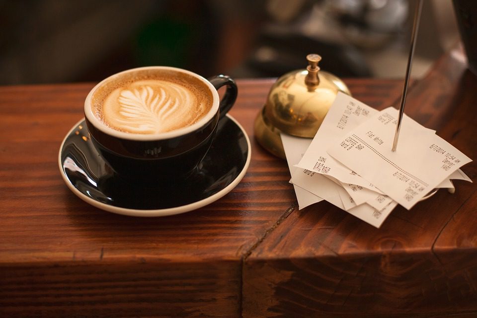 A cup of coffee next to a bell and paper orders