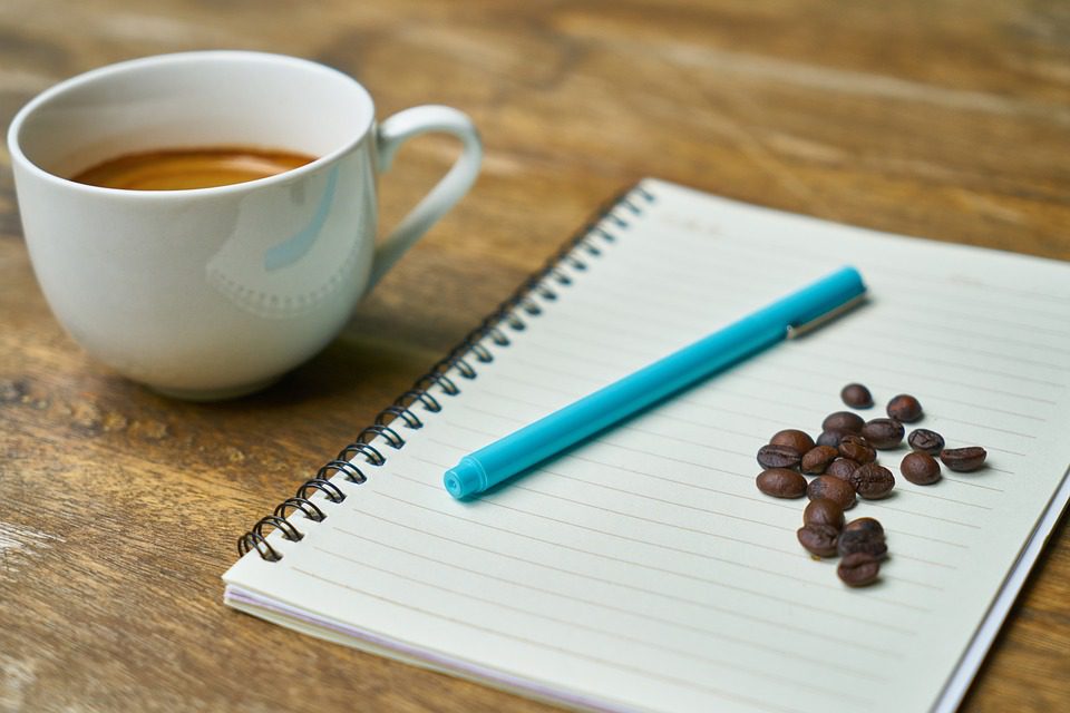 A pen and paper with a cup of coffee and some beans