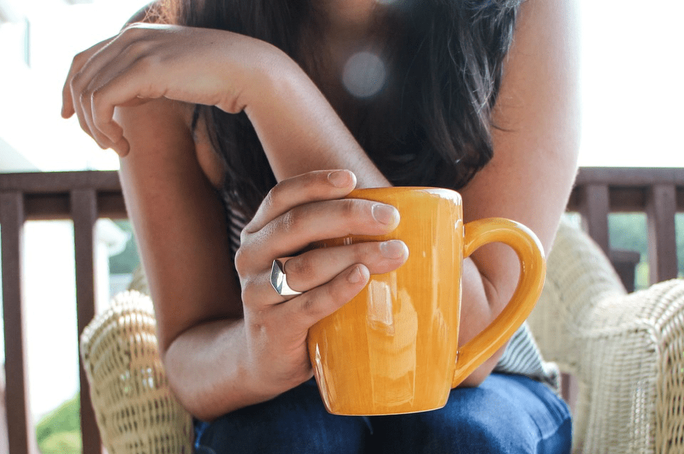A healthy woman holding a yellow coffee cup outside in the sun