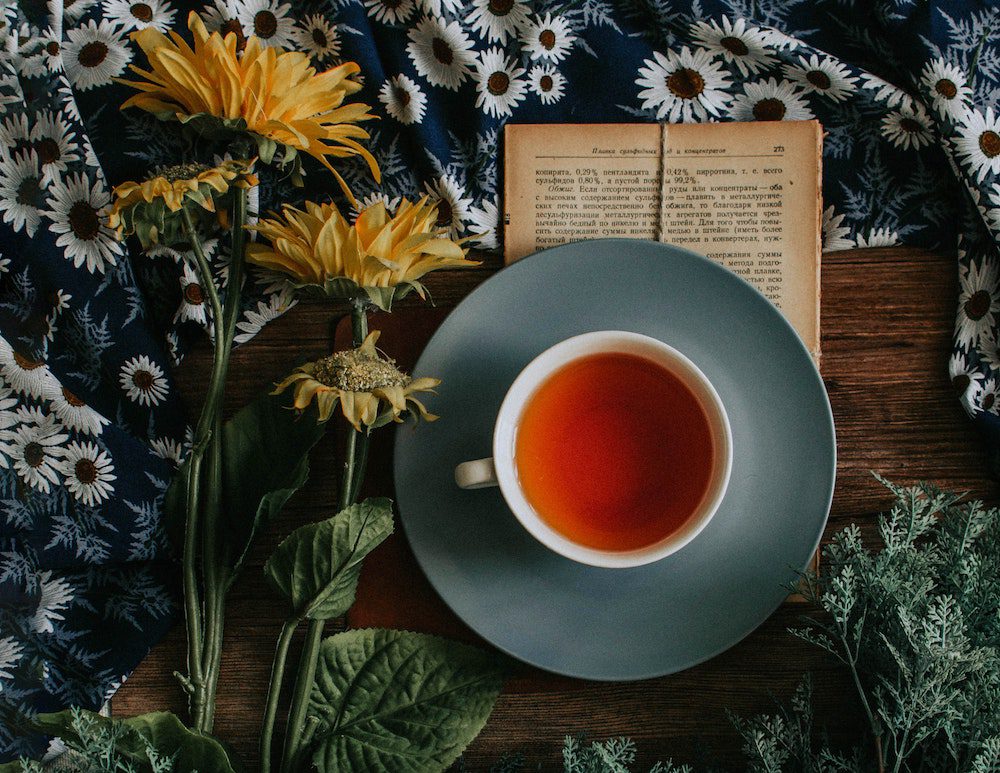cup of tea on table with book and flowers