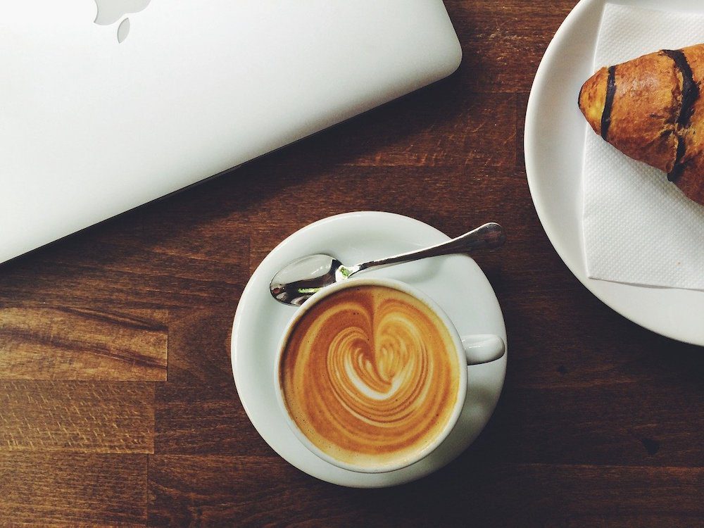 A laptop, croissant and cup of coffe on a table