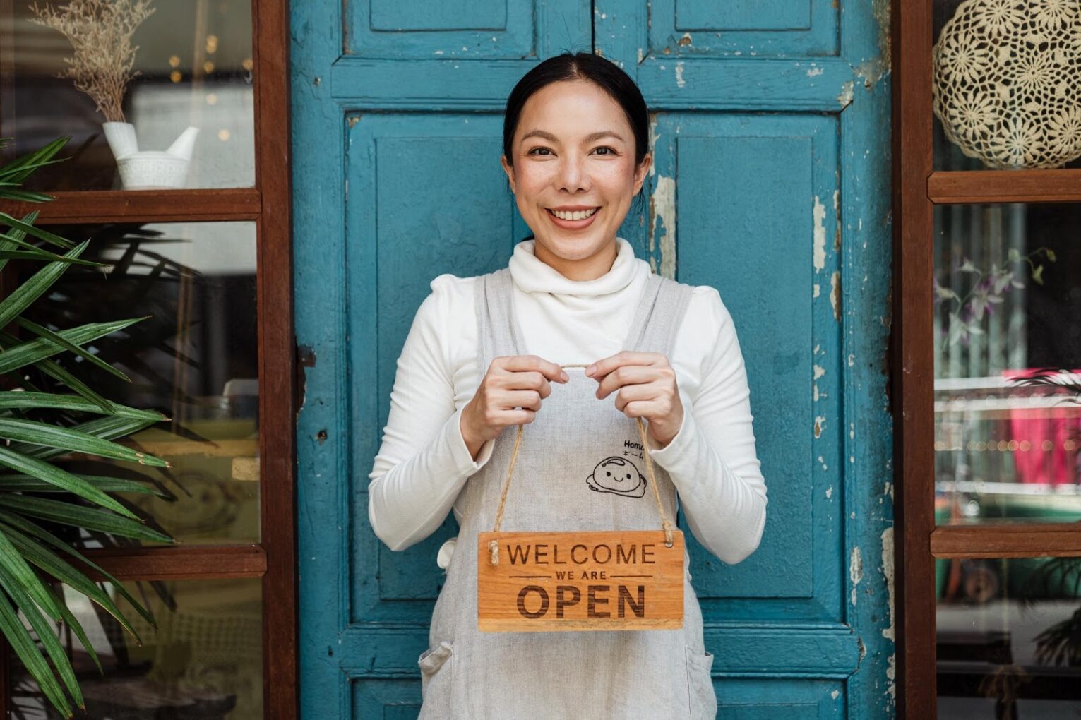 A woman holding an ‘open’ sign in front of a door