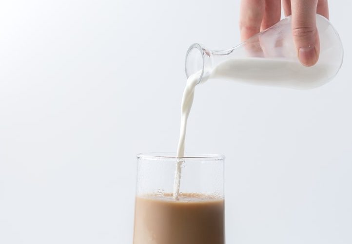 Someone pouring milk into a drink
