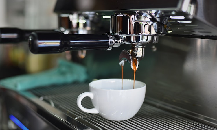 An espresso machine pouring coffee into a white mug