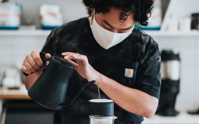 A barista pouring coffee while wearing a face-covering 
