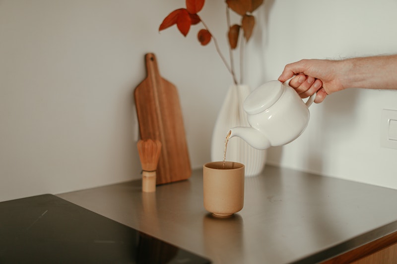 Someone pouring tea into a cup from a white teapot