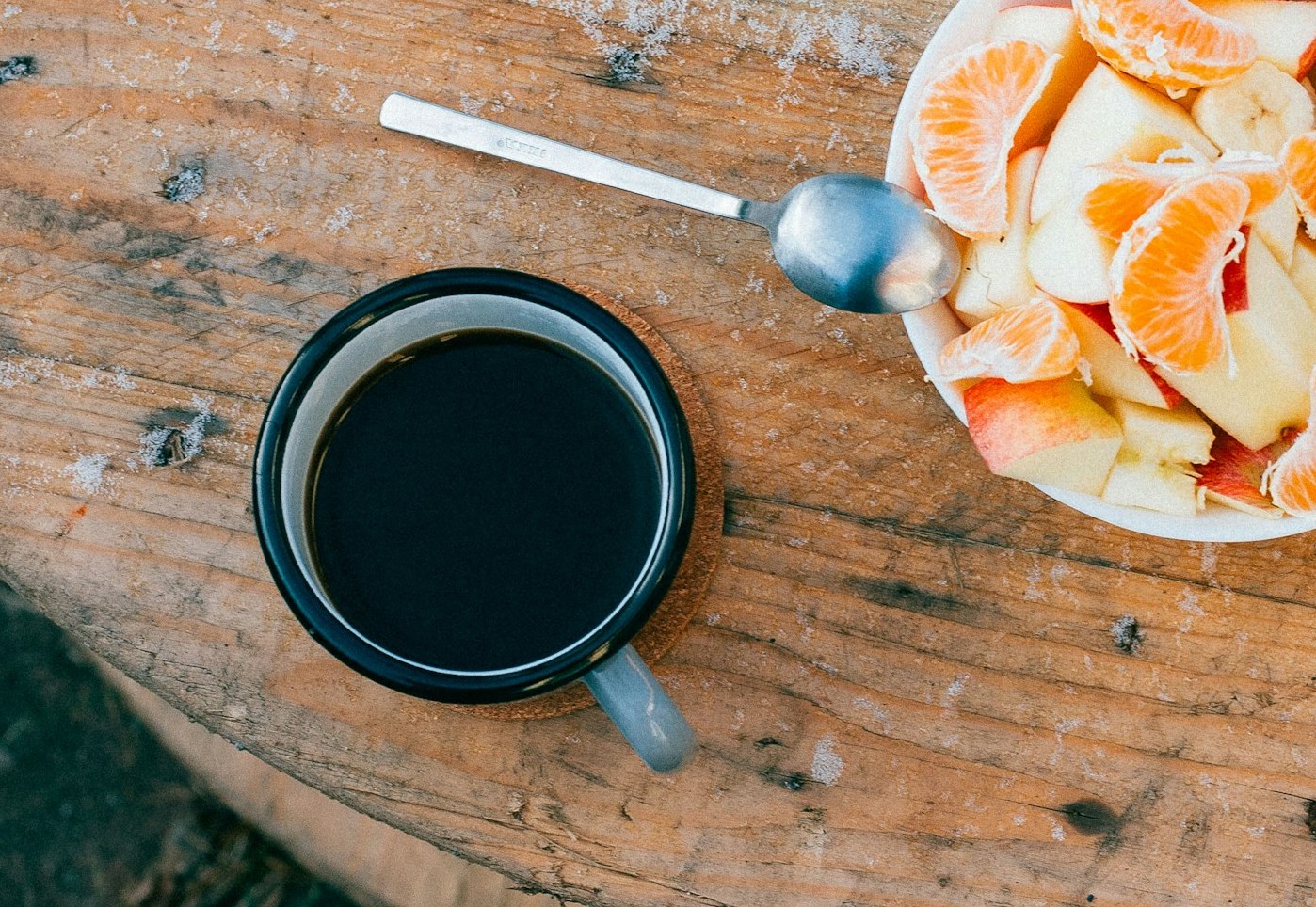 A bowl of oranges and apples next to a cup of black coffee