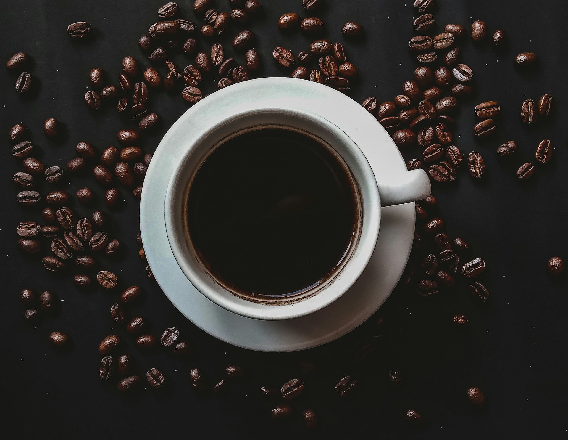 Black coffee in a white cup surrounded by coffee beans