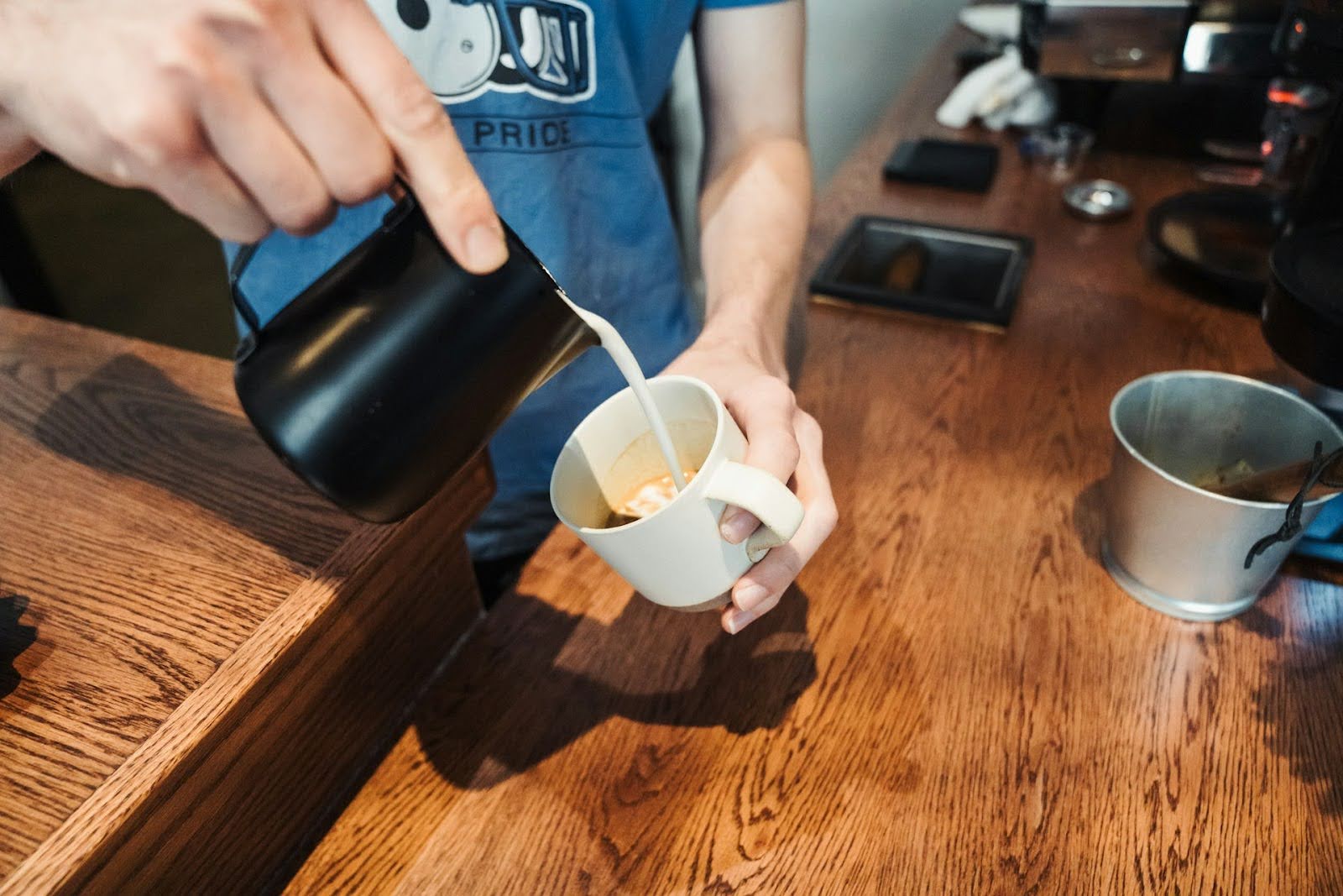 Barista pouring milk into a white coffee cup